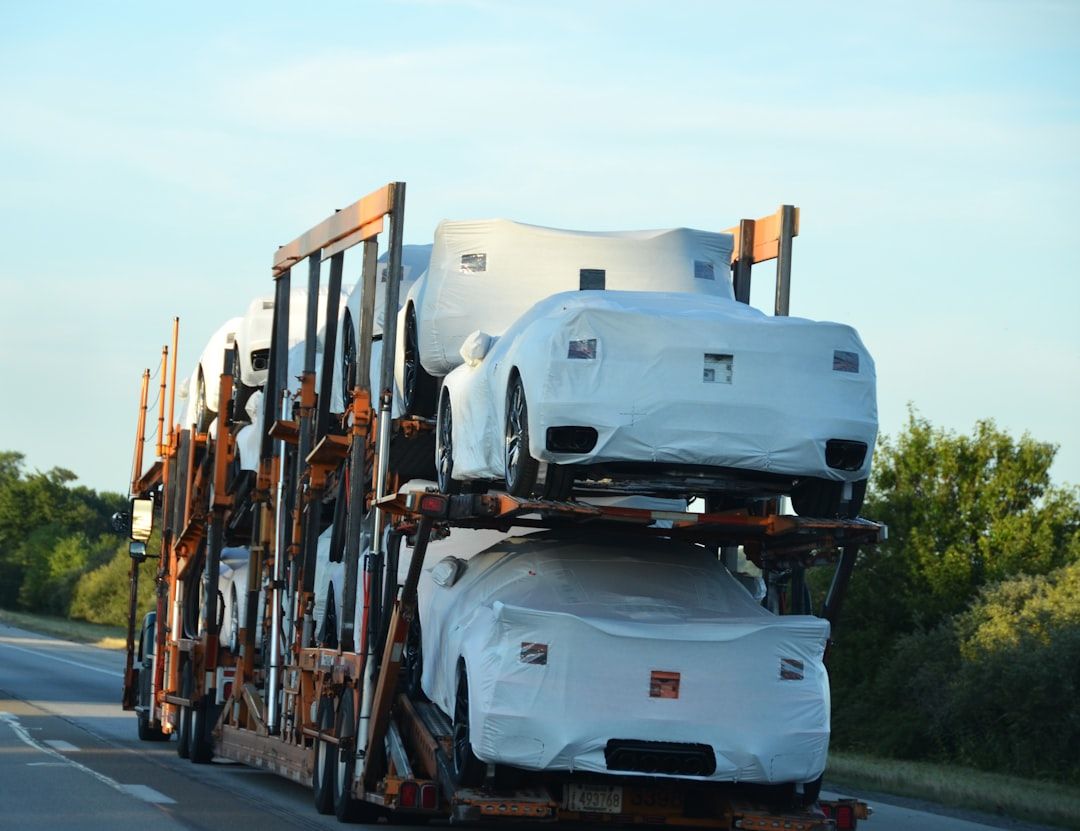Ein Autotransporter beladen mit weiß verhüllten Neuwagen auf einer Straße.