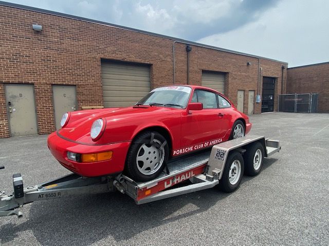 Roter Porsche auf einem Pkw-Anhänger vor einem Backsteingebäude.