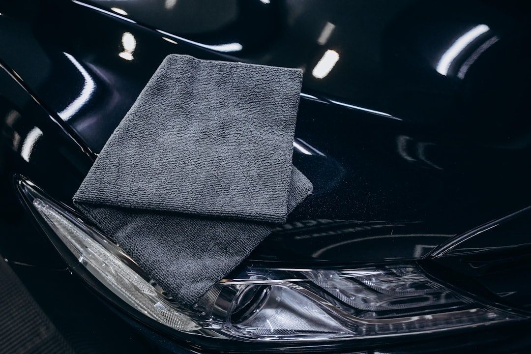 Graues Mikrofasertuch liegt auf dem glänzenden Lack eines schwarzen Autos